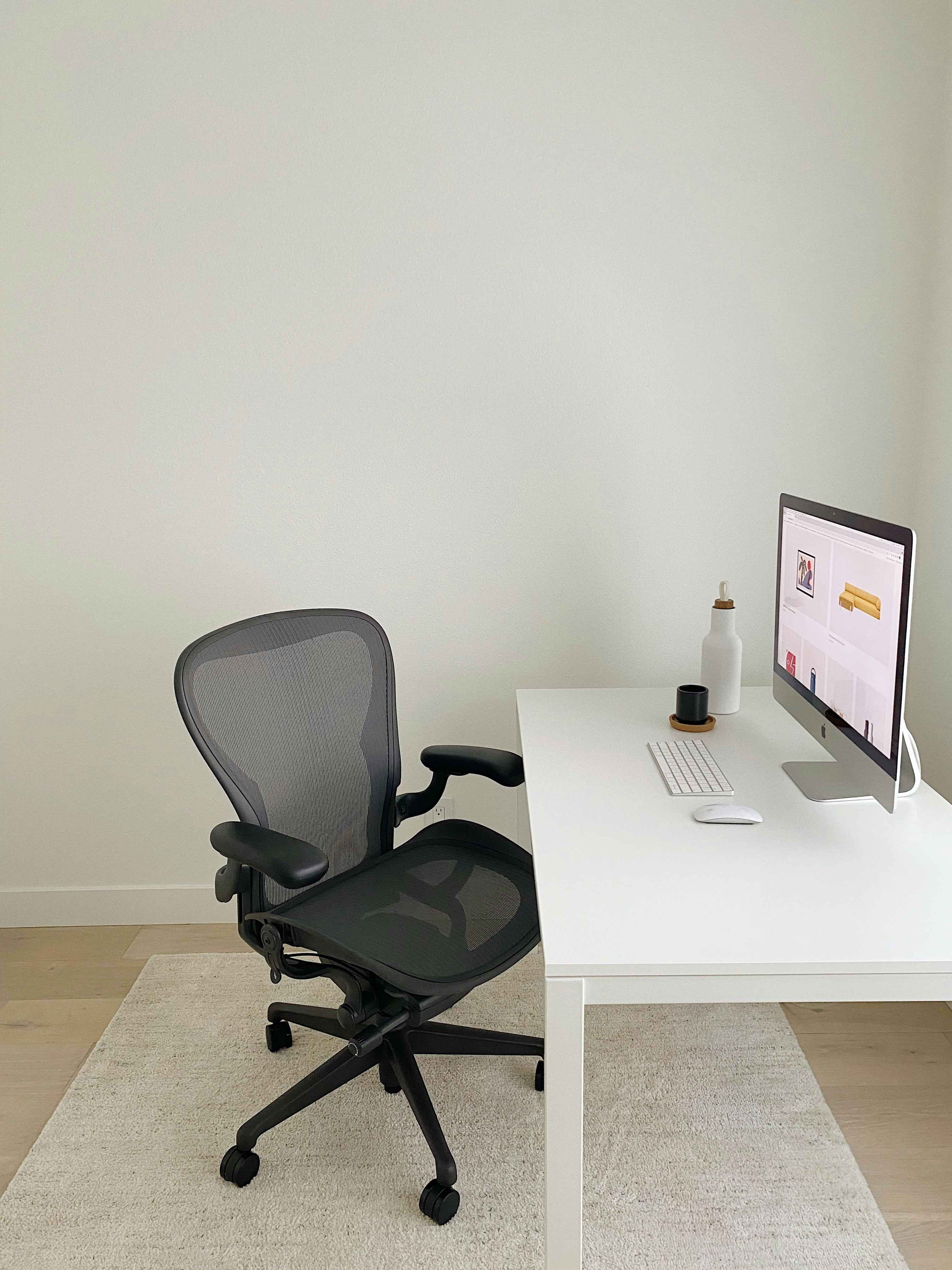 Minimalist workspace with wooden clock, white desk lamp, and small plant on clean desk - representing calm and professional design aesthetic